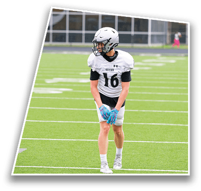 A person wearing a white football uniform and helmet stands on a green football field looking to the side. Description generated by AI