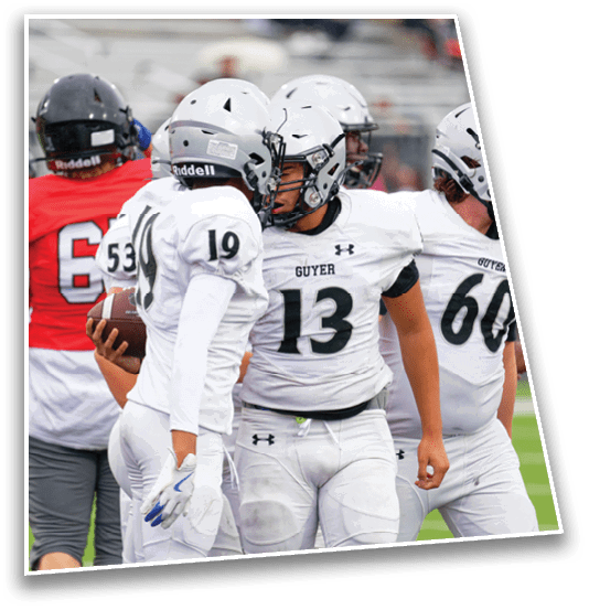 Two people in white football uniforms are celebrating on the field while other players in red and gray uniforms walk away in the background. Description generated by AI
