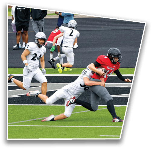 A person in a red jersey and black helmet is running with a football while being tackled by a person in a white jersey on a green and black football field. Description generated by AI