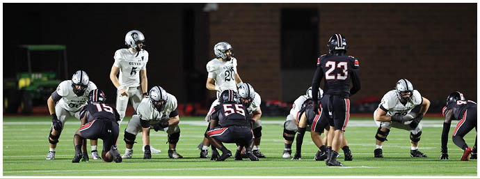 People in football uniforms are lined up on a field preparing for a play during a game. Description generated by AI