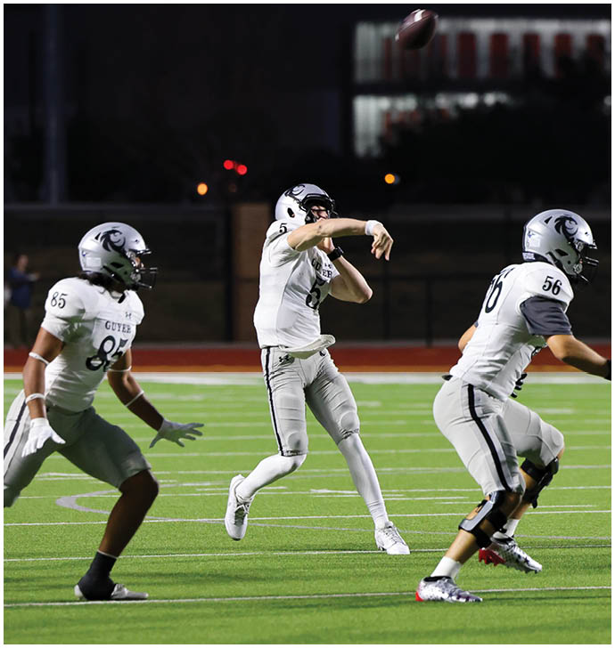 Three people in white football uniforms are on a field at night with one person throwing a football. Description generated by AI