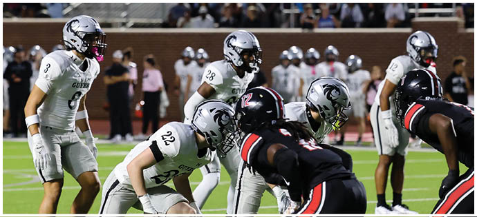 Players from two opposing football teams are lined up on the field preparing for a play during a game. Description generated by AI