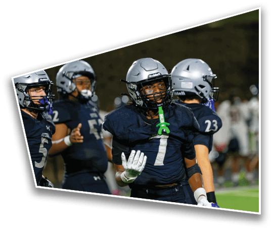 People wearing football helmets and uniforms are standing on a field during a game or practice at night. Description generated by AI
