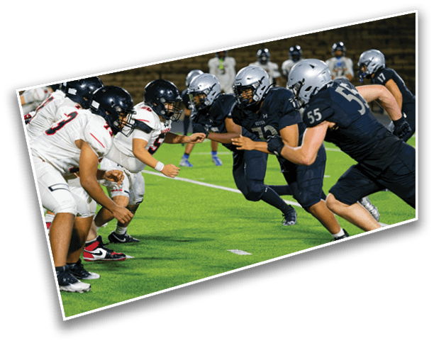 Two opposing American football teams in dark and white uniforms are lined up facing each other on a green field, ready for a play. Description generated by AI