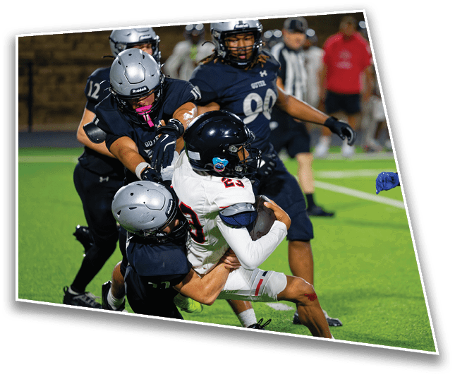 Two people in football uniforms are engaged in a tackle on a green field during a game. Description generated by AI