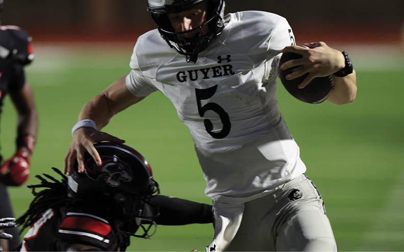 A person wearing a white football uniform with the word “GUYER" and a helmet is running while holding a football. Description generated by AI