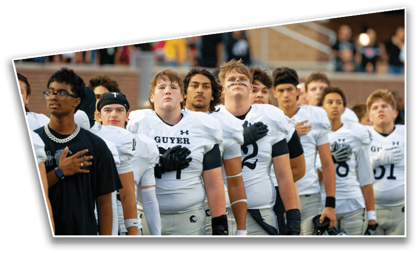 A group of people wearing football uniforms and one person in a black shirt stand in a line with their hands over their hearts, likely during a national anthem at a sports event. Description generated by AI