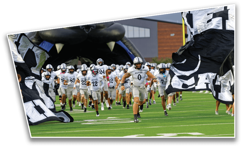 A group of people in white sports uniforms is running onto a football field through large black and white flags and an inflatable tunnel. Description generated by AI