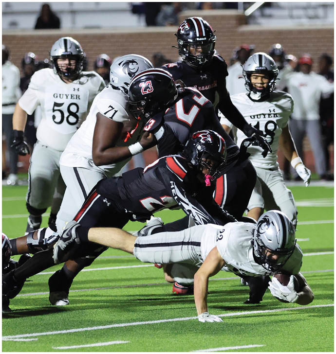 A group of football players in black and white uniforms are engaged in a tackle on a green field during a game. Description generated by AI
