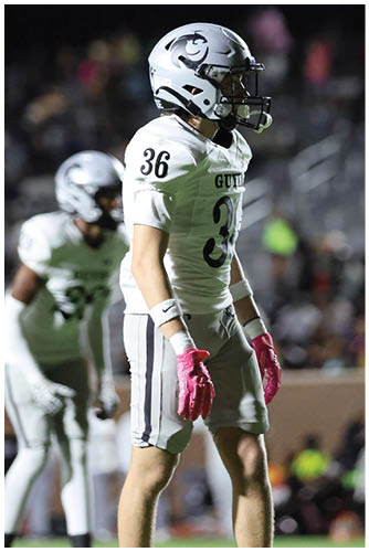 Two people wearing white football uniforms and helmets are on a field at night with a blurred crowd in the background. Description generated by AI