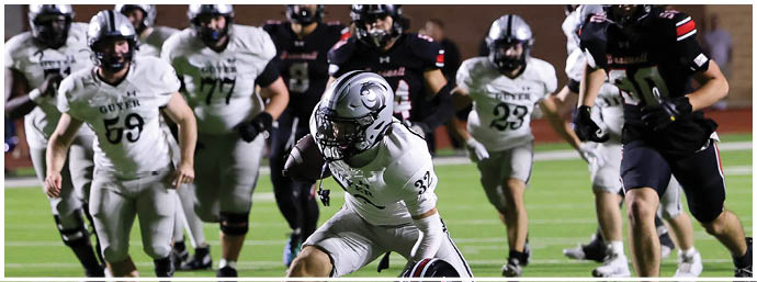 A group of people in football uniforms are actively playing on a field with one person in white tackling another person in black. Description generated by AI