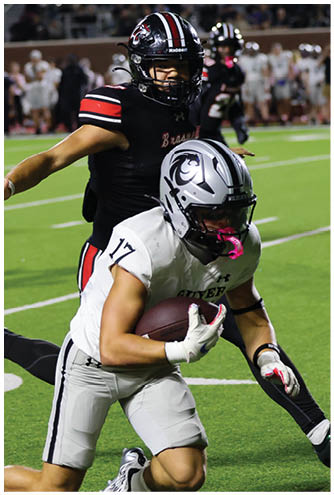 A person in a white football uniform with the number 17 is running with the ball while another person in a black football uniform attempts to tackle them on a green field during a game. Description generated by AI