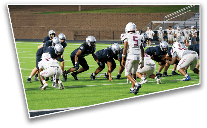 A group of people in football uniforms are lined up on a green field preparing for a play near the end zone. Description generated by AI
