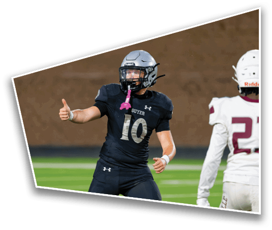 A person wearing a black football uniform with the number 10 is giving a thumbs-up on a football field while another person in a white uniform stands nearby. Description generated by AI