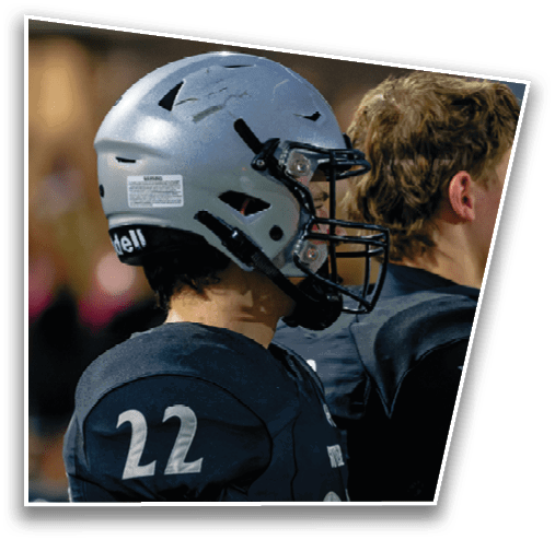 A person wearing a silver football helmet and a dark jersey with the number 22 is standing on a field with blurred people in the background. Description generated by AI