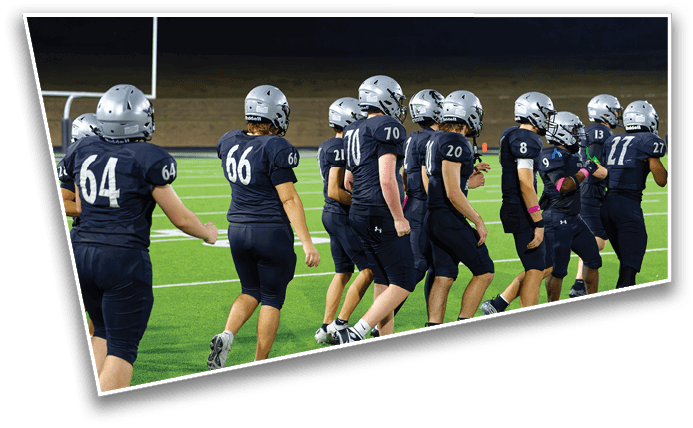 A group of people wearing dark sports uniforms and silver helmets are walking together on a football field at night. Description generated by AI