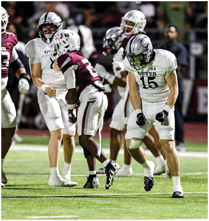 People wearing football uniforms are engaged in a game on a field with a blurred crowd in the background. Description generated by AI