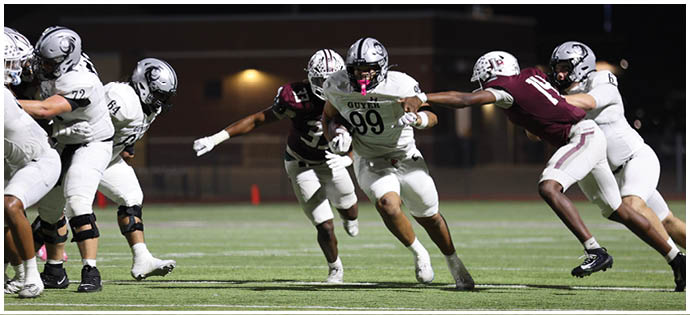 People in football uniforms are actively engaged in a play on a lit field during a nighttime game. Description generated by AI