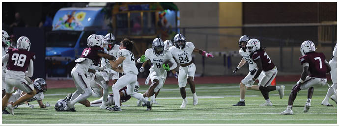 A group of people wearing football uniforms are actively playing on a field with one person running while holding a football and others preparing to block or tackle. Description generated by AI