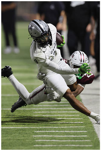 A person in white football gear is diving forward while holding a football as another person in maroon and white gear attempts to tackle them on a football field. Description generated by AI