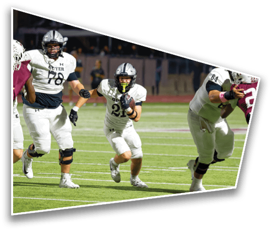 Three people in football uniforms are actively running on a field during a game, with one person holding a football and others appearing to block or chase. Description generated by AI