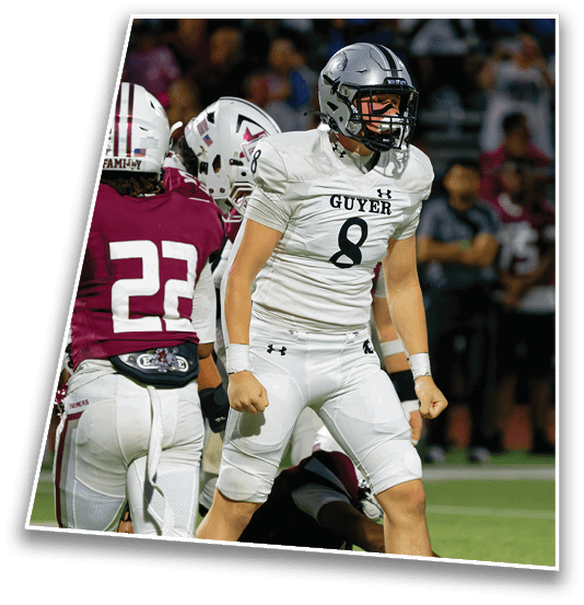 A person wearing a white football uniform with the number 8 is standing on a football field looking intense while other players in maroon and white uniforms are nearby. Description generated by AI