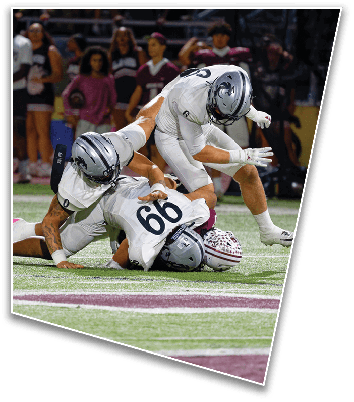 Two people in football uniforms are on the ground during a game, with one person tackling the other who is wearing a helmet and jersey number 66. Description generated by AI
