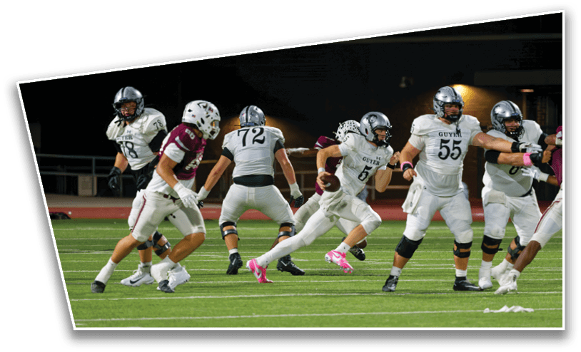 People in football uniforms are actively playing on a field at night with one person running with the ball while others are positioned around them. Description generated by AI