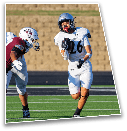 Two people in football uniforms are engaged in a tackle on a green field with a blurred background. Description generated by AI