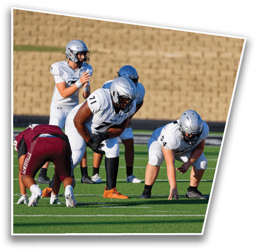 People in football uniforms are positioned on a field preparing for a play during a game. Description generated by AI