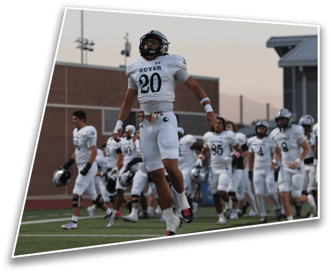 A group of people in white football uniforms are on a field with one person in the foreground jumping or celebrating. Description generated by AI