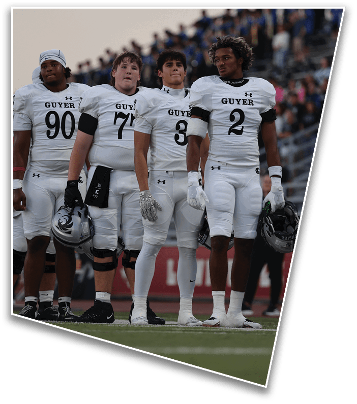 Four people in white football uniforms with the word “GUYER" stand side by side on a field with a crowd in the background. Description generated by AI