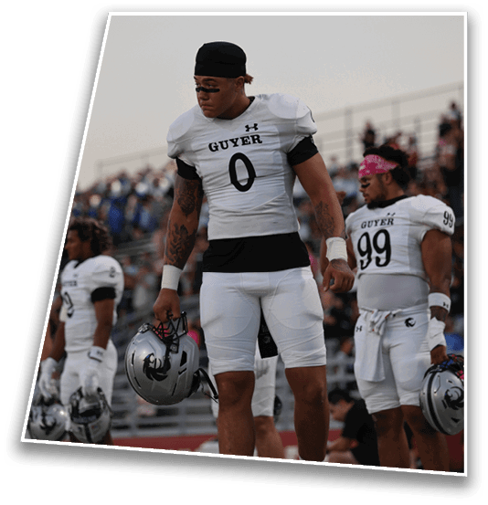 A person wearing a white football jersey with the word “GUYER" and the number zero is looking to the side while standing outdoors against a clear sky. Description generated by AI