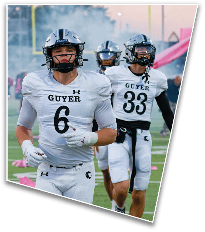 Three people in white football uniforms with helmets are walking on a field with goalposts and smoke in the background. Description generated by AI