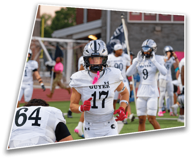 Several people in white football uniforms with helmets are on a field, with one person wearing number 17 running toward the camera and others standing or walking in the background. Description generated by AI