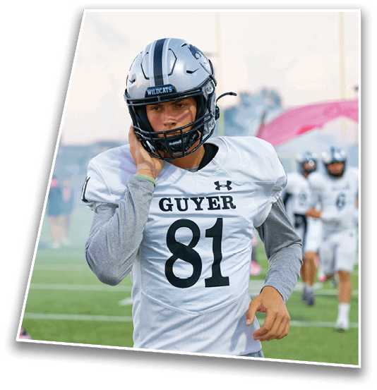 A person wearing a football uniform with the number 81 and the word “GUYER" on the jersey is walking on a football field while holding their helmet. Description generated by AI