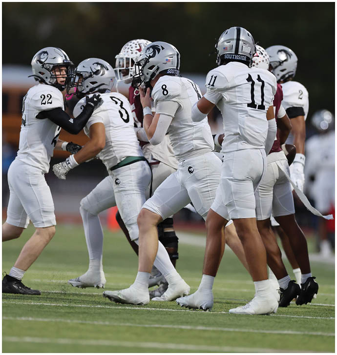 A group of football players in white uniforms and helmets are gathered closely on a field, appearing to prepare for a play. Description generated by AI