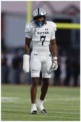 Two people in white football uniforms stand on a field with one person wearing a glove on one hand and a mouthguard. Description generated by AI