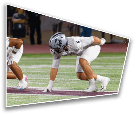 Two people in white football uniforms and helmets are crouched in a ready position on a football field. Description generated by AI