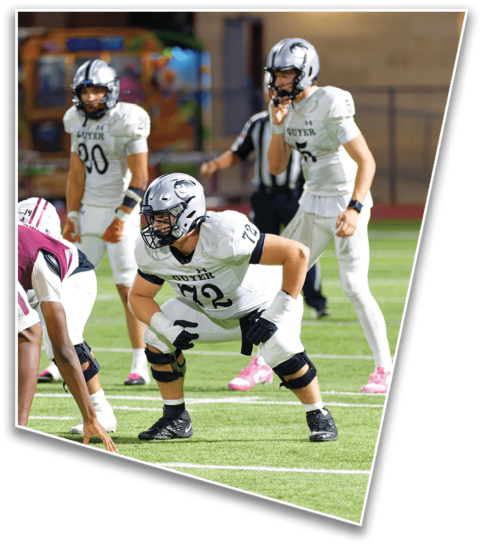 People in football uniforms are positioned on a field preparing for a play during a game. Description generated by AI