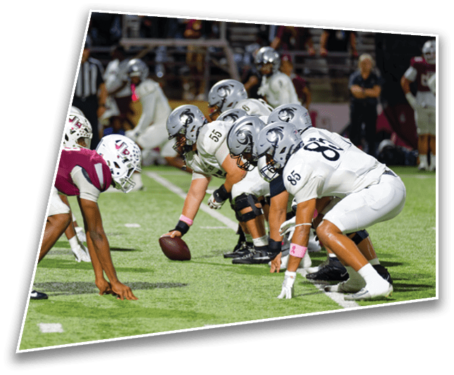 Two opposing football teams are lined up at the line of scrimmage on a field, ready for the next play. Description generated by AI