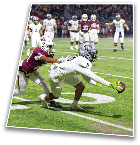 Two football players in action on a field with one player in white reaching out to catch or recover the ball while being closely pursued by a player in maroon. Description generated by AI