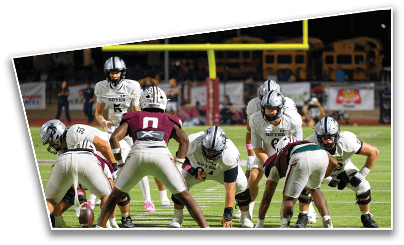 People in football uniforms are positioned on a field preparing for a play during a nighttime game. Description generated by AI