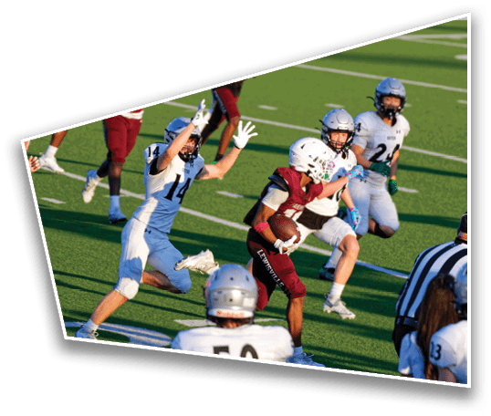 A person in a maroon football uniform is running with the ball while several people in white football uniforms and helmets are attempting to catch them on a green field. Description generated by AI
