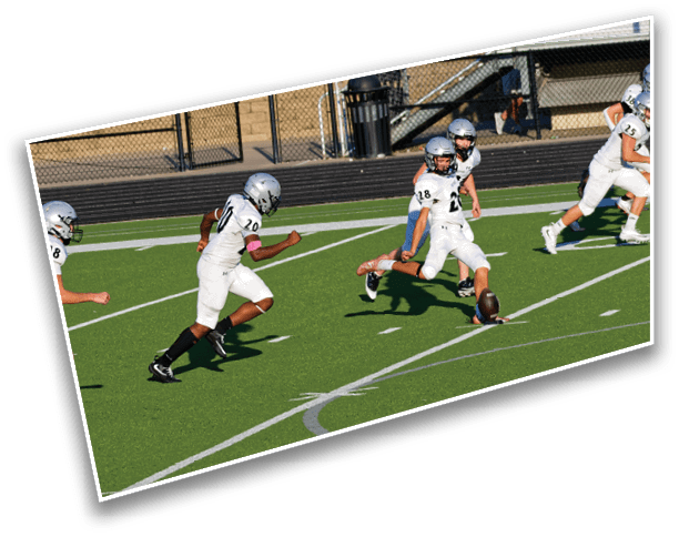 Four people in white football uniforms and helmets are running on a green field toward a football on the ground. Description generated by AI