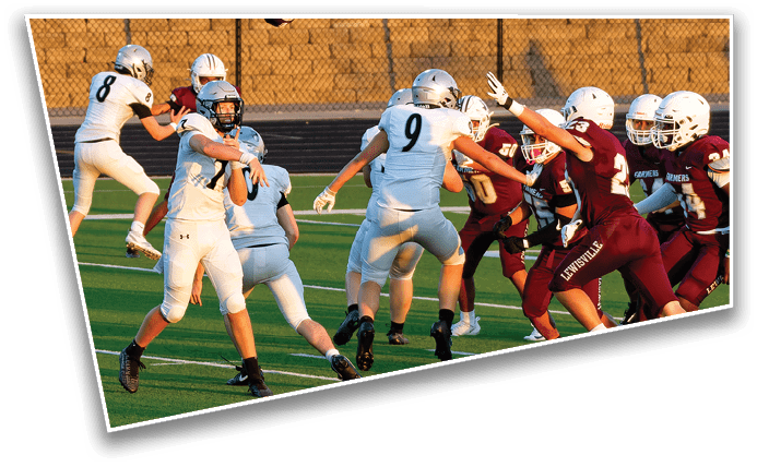 People in football uniforms are actively engaged in a game on a green field with one person preparing to throw a football while others are running and blocking. Description generated by AI