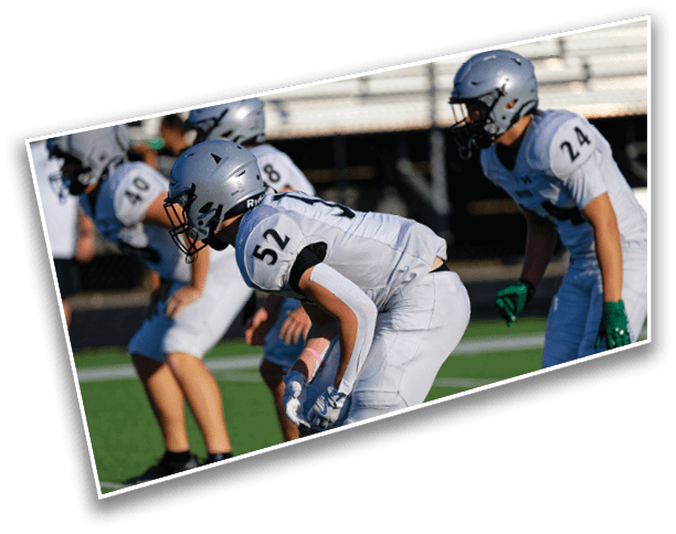 People in football uniforms and helmets are crouched in a ready position on a green field during a game or practice. Description generated by AI