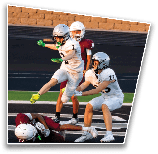 Two people wearing football helmets and uniforms are engaged in a game with a brick wall in the background. Description generated by AI