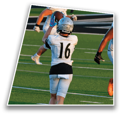 Two people wearing football helmets and uniforms are on a field, with one person holding a football and the other giving a thumbs-up gesture. Description generated by AI