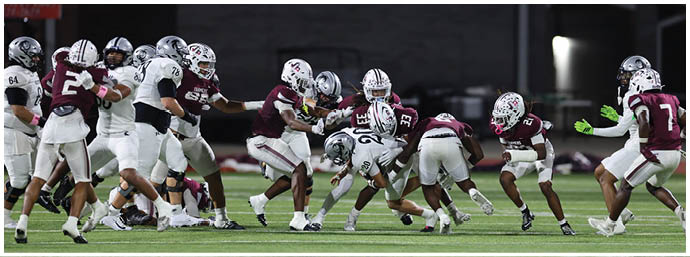 People wearing football uniforms are actively engaged in a play on a green field during a game. Description generated by AI